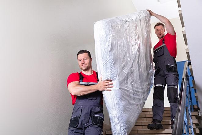 a heavy box spring being carried out of a house in Bellerose